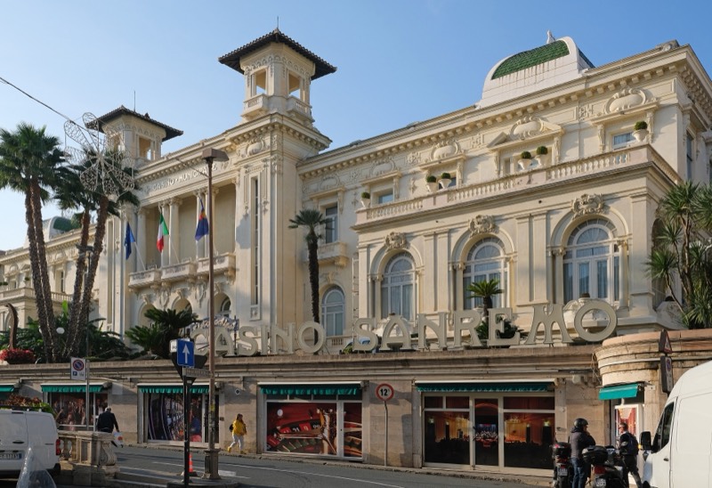 Facciata bianca in stile Liberty del Casinò di Sanremo illuminata dal sole, con palme