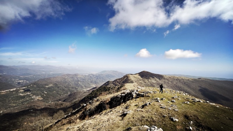 Escursionista sul crinale erboso del Pizzo d'Evigno con vista sulle valli del Ponente ligure